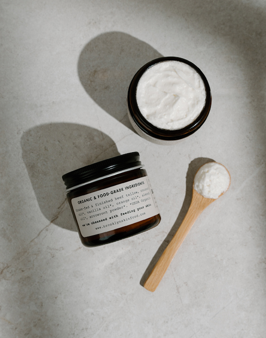 Two jars of cream with a spoonful of cream on a textured surface