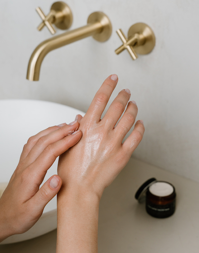 Person applying soap to hands under a gold faucet in a bathroom setting