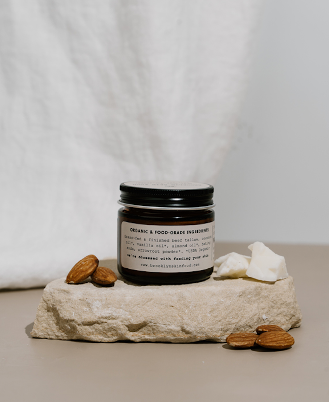 Jar of organic product on a stone surface with almonds and a white cloth in the background
