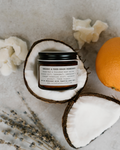 Jar of organic product on a coconut half with oranges and flowers on a textured surface