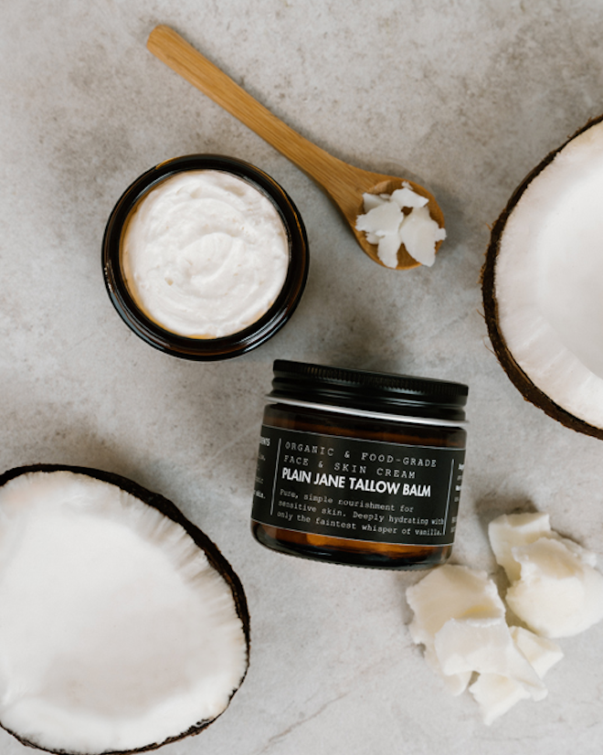 Plain Jane Tallow Balm jar with a spoonful of balm and coconut halves on a neutral background